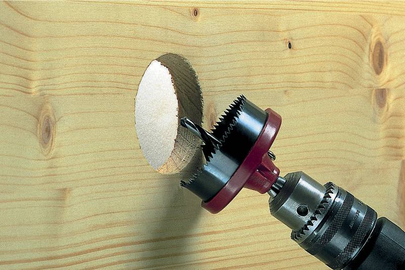 Bohrer mit Lochsäge schneidet ein kreisrundes Loch in ein Holzbrett.