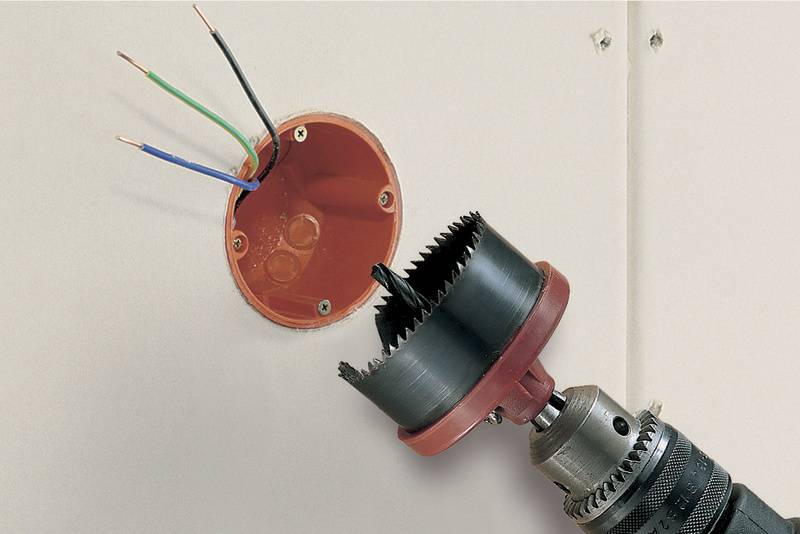 Nahaufnahme einer Bohrmaschine mit Lochsäge, die ein rundes Loch in eine Wand schneidet, um eine Elektroinstallationsdose einzusetzen.