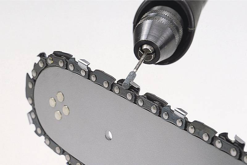 Ein Bohrer schärft die Kette einer Kettensäge. Nahaufnahme zeigt präzise Ausrichtung der Kettenglieder.