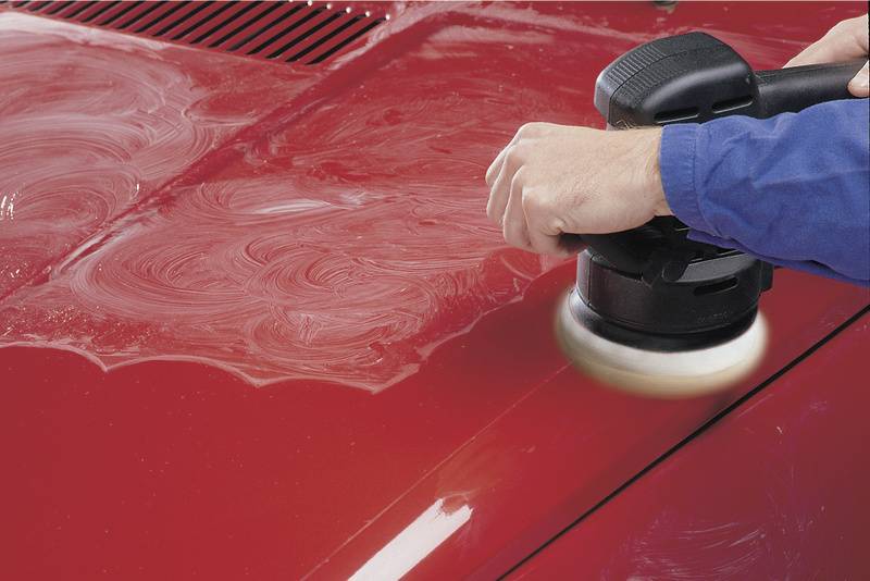 Eine Person poliert eine rote Autokarosserie mit einer elektrischen Poliermaschine.