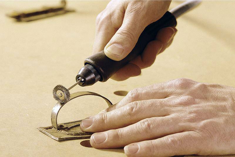 Eine Person benutzt ein Handwerkzeug, um Metall zu bearbeiten. Das Werkzeug schneidet einen kreisförmigen Ausschnitt in eine Metallplatte.