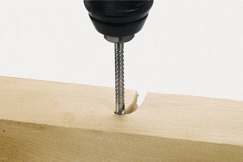 Eine Bohrmaschine mit einem gefrästen Bohrer bearbeitet ein rechteckiges Holzstück mit einer Kante.