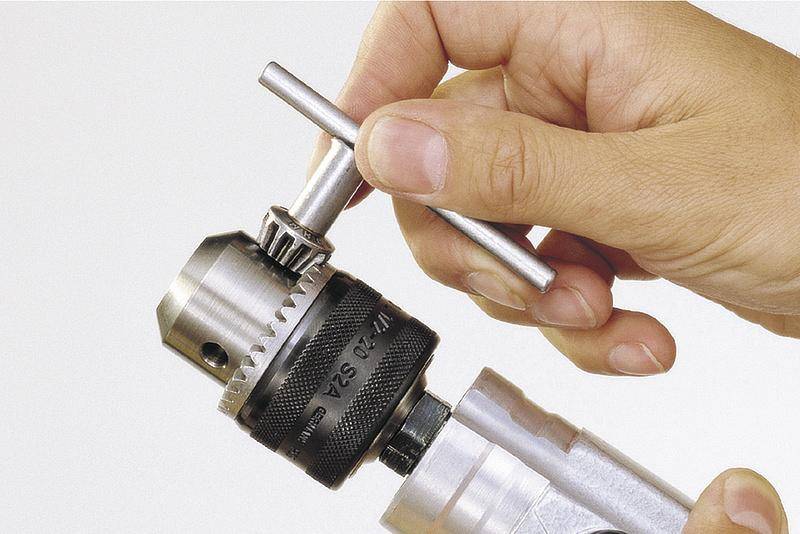 Eine Hand hält einen Schlüssel und spannt ein Bohrfutter an einer Bohrmaschine, um den Bohrer zu fixieren.