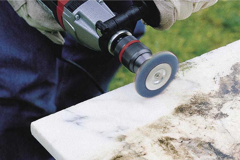 Eine Person poliert mit einem rotierenden Werkzeug eine weiße Marmorkante. Die Oberfläche zeigt vorher und nachher den Reinigungseffekt.