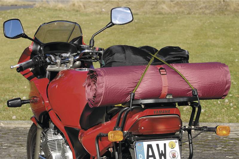 Ein rotes Motorrad mit einem auf dem Gepäckträger befestigten Zelt. Das Motorrad steht auf einer gepflasterten Fläche im Freien.