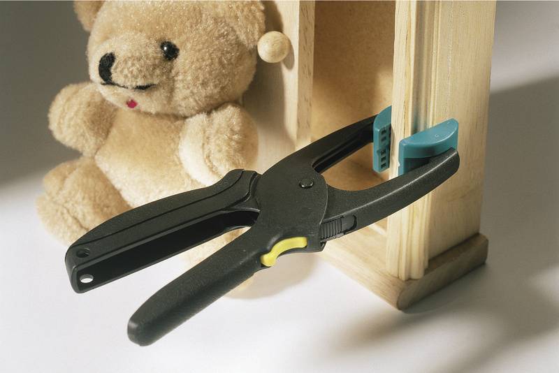 Ein schwarzer Schraubzwinge hält ein Holzstück neben einem Plüschtier. Der Hintergrund ist weiß.