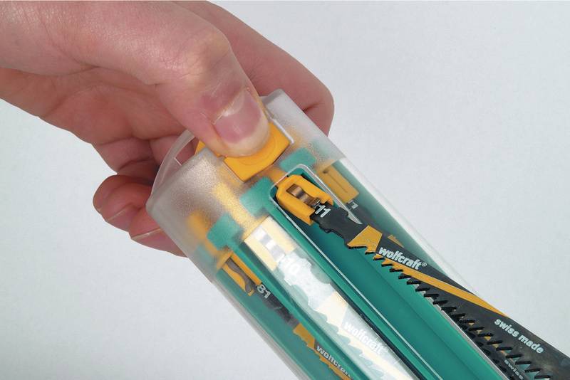 Hand öffnet Kunststoffverpackung mit verschiedenen Sägeblättern. Die Sägeblätter sind in einer transparenten Röhre aufbewahrt.