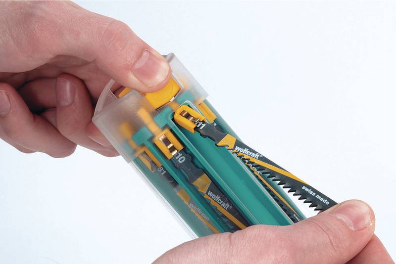 Zwei Hände halten einen zylindrischen Behälter mit verschiedenen Sägeblättern. Eine Hand dreht den Verschluss oben am Behälter.