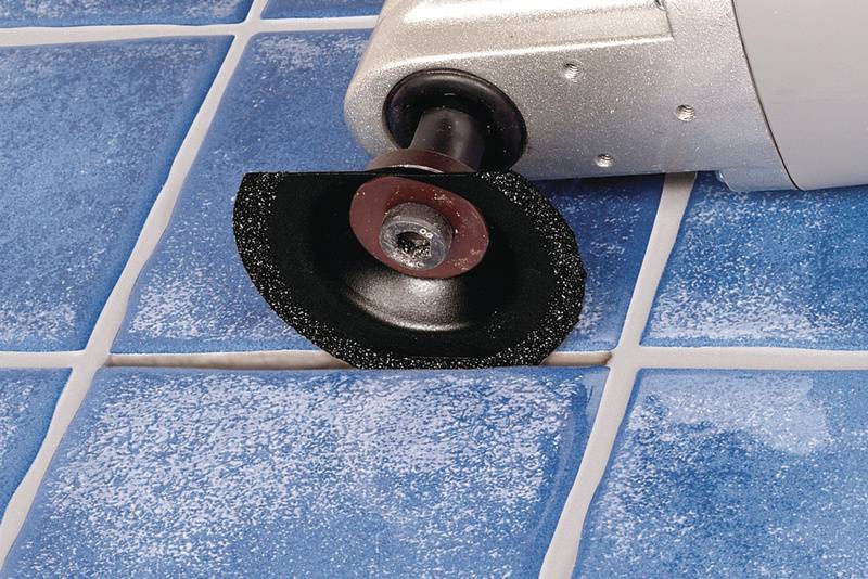 Eine elektrische Fliesenschneidemaschine schneidet eine blaue Keramikfliese. Die Klinge bewegt sich durch eine Fliesenlinie.