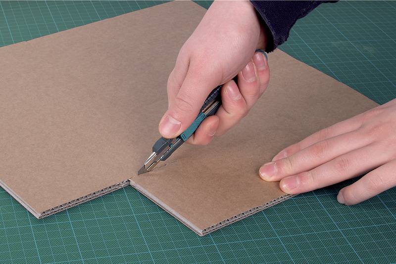 Eine Person schneidet mit einem Cutter-Messer einen Karton auf einer Schneidematte.