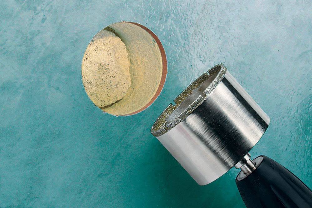 Ein Metallbohrer entfernt einen zylindrischen Abschnitt aus einer blauen Betonoberfläche, Bohrstaub liegt auf der Schnittfläche.