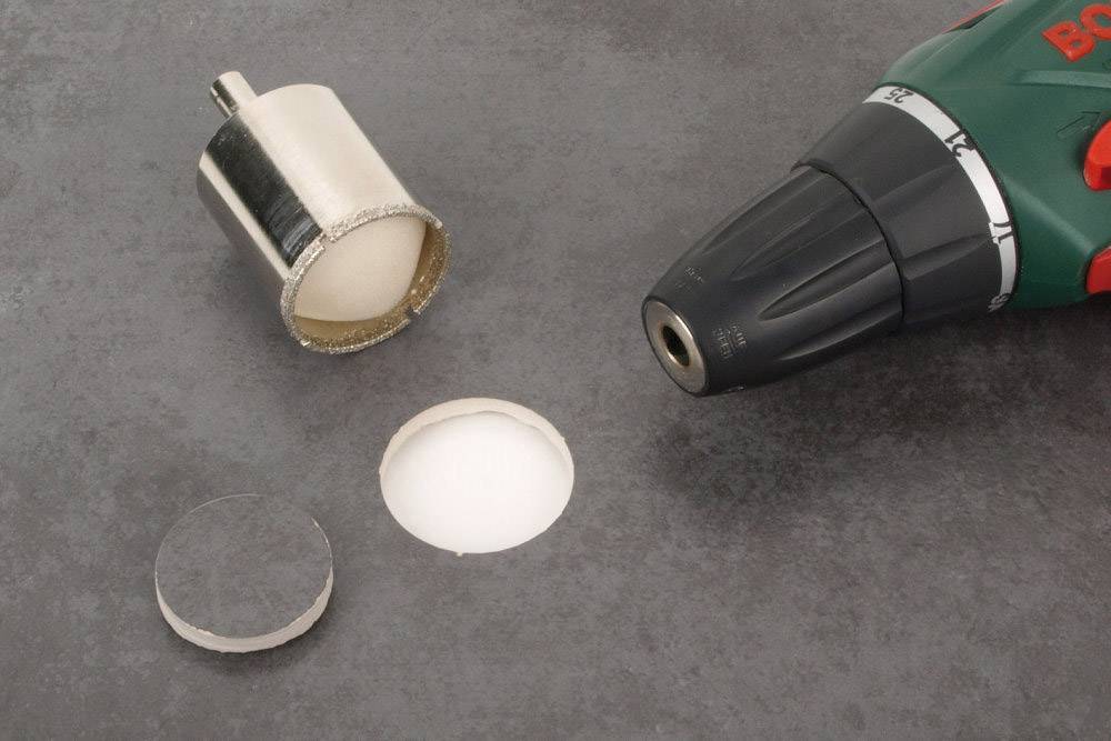 Bohraufsatz neben einem Bohrer, verwendet zum Ausschneiden eines runden Teils aus einer glatten Oberfläche.