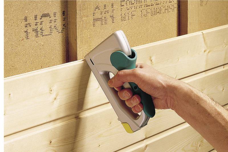 Eine Hand hält einen Tacker und befestigt Holzpaneele an einer Wand.