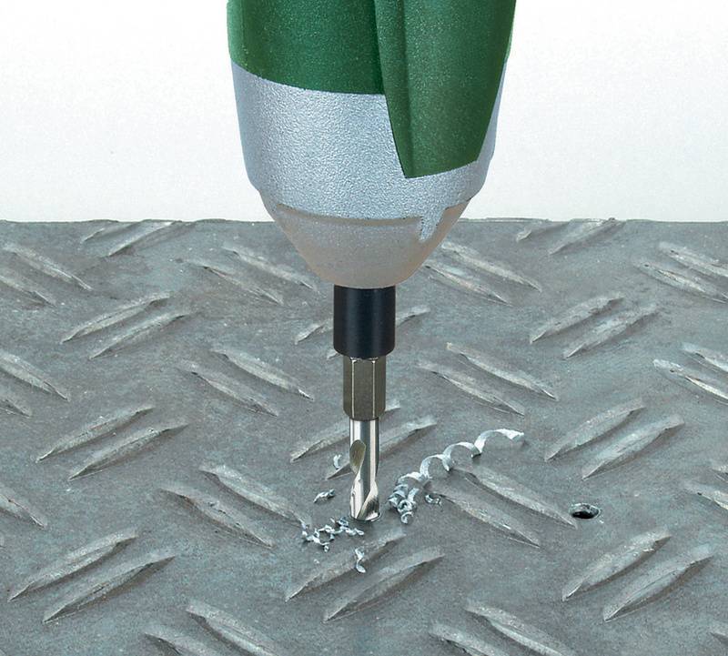 Ein grüner elektrischer Bohrer bohrt ein Loch in eine Metallplatte mit Diamant-Riffelung, umgeben von Metallschraubspänen.