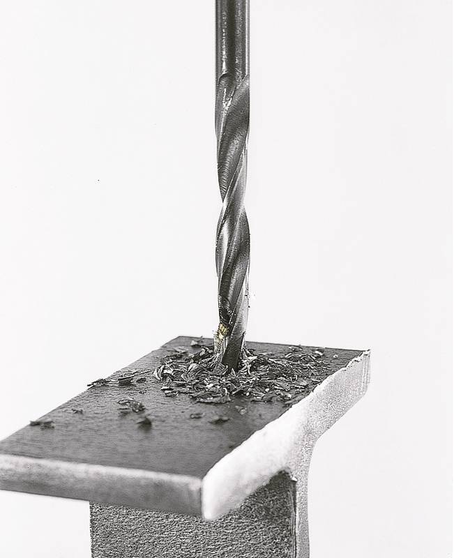 Ein Bohrer durchbohrt ein Metallstück. Metallspäne sind auf der Oberfläche verstreut.