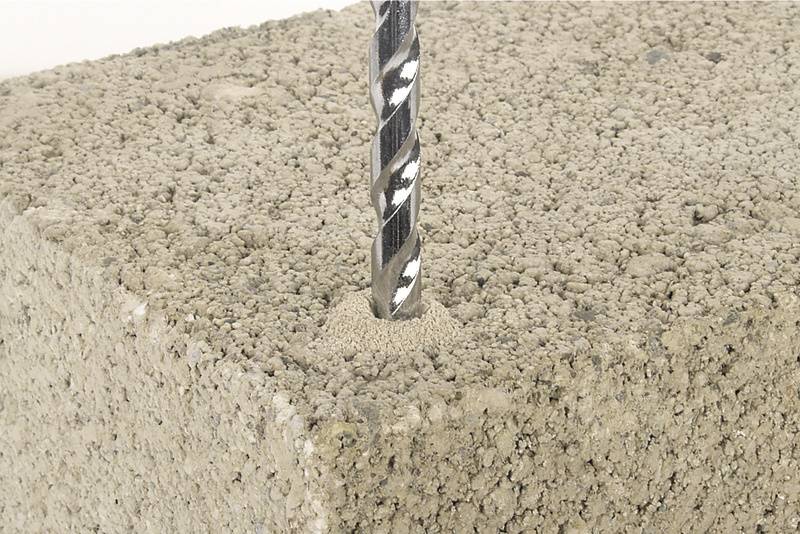 Ein Bohrer dringt in einen porösen Betonblock ein. Nahaufnahme zeigt den Bohrvorgang und die Struktur des Baustoffs.