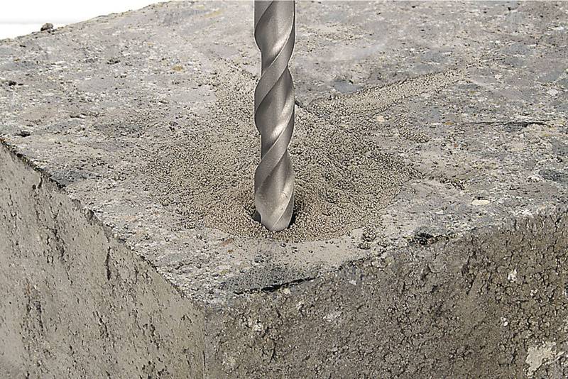 Bohrer dringt in rauen Betonblock ein, während Staub um das Bohrloch verstreut ist.