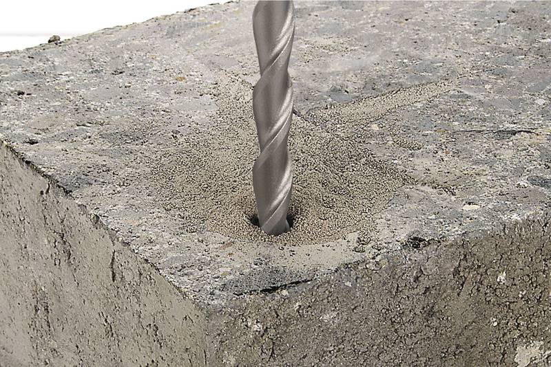 Ein Bohrer dringt in einen Betonblock ein und erzeugt Bohrstaub um das Loch.