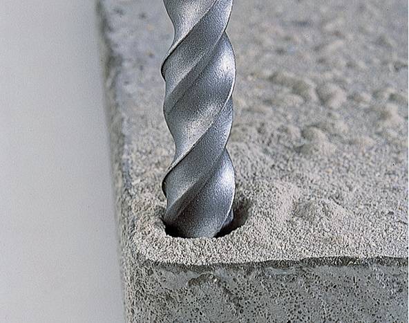 Ein Bohrer dringt in einen Betonblock ein. Die silberne Bohrspitze erzeugt ein neues Loch in der rauen, grauen Oberfläche.