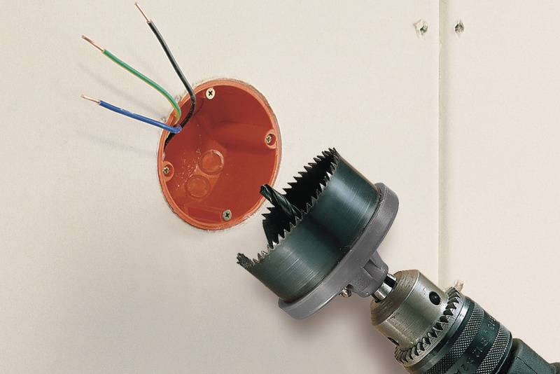 Bohrwerkzeug erstellt eine runde Öffnung in einer Wand, um eine Unterputzdose zu installieren, aus der Kabel ragen.