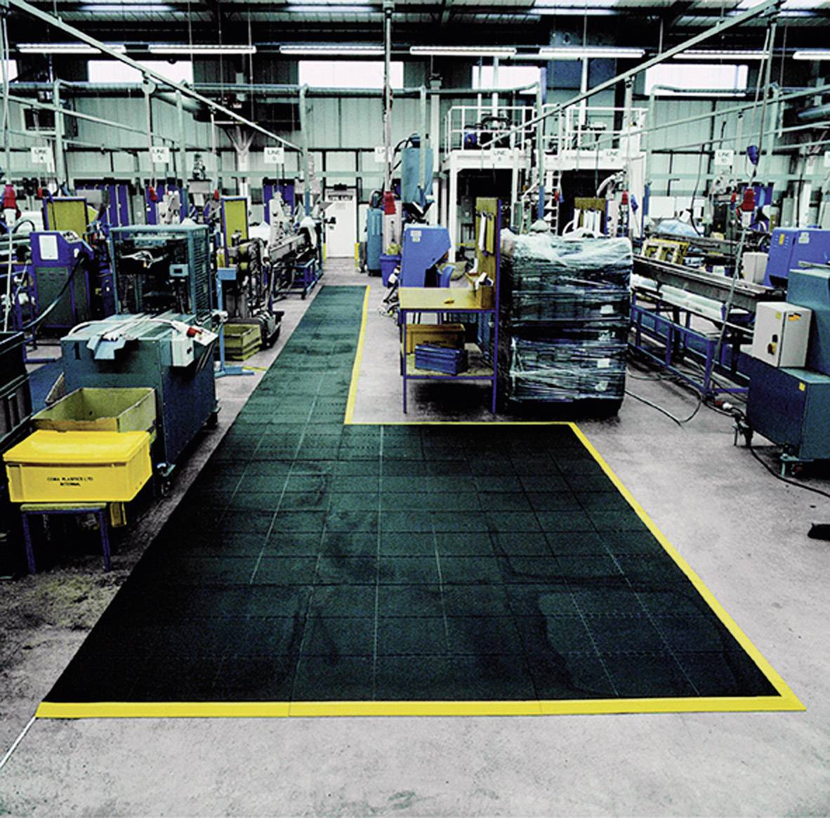 Große Industriehalle mit Maschinenreihen und gekennzeichnetem Gehweg aus rutschfestem Material, geschützt durch gelbe Markierungen.