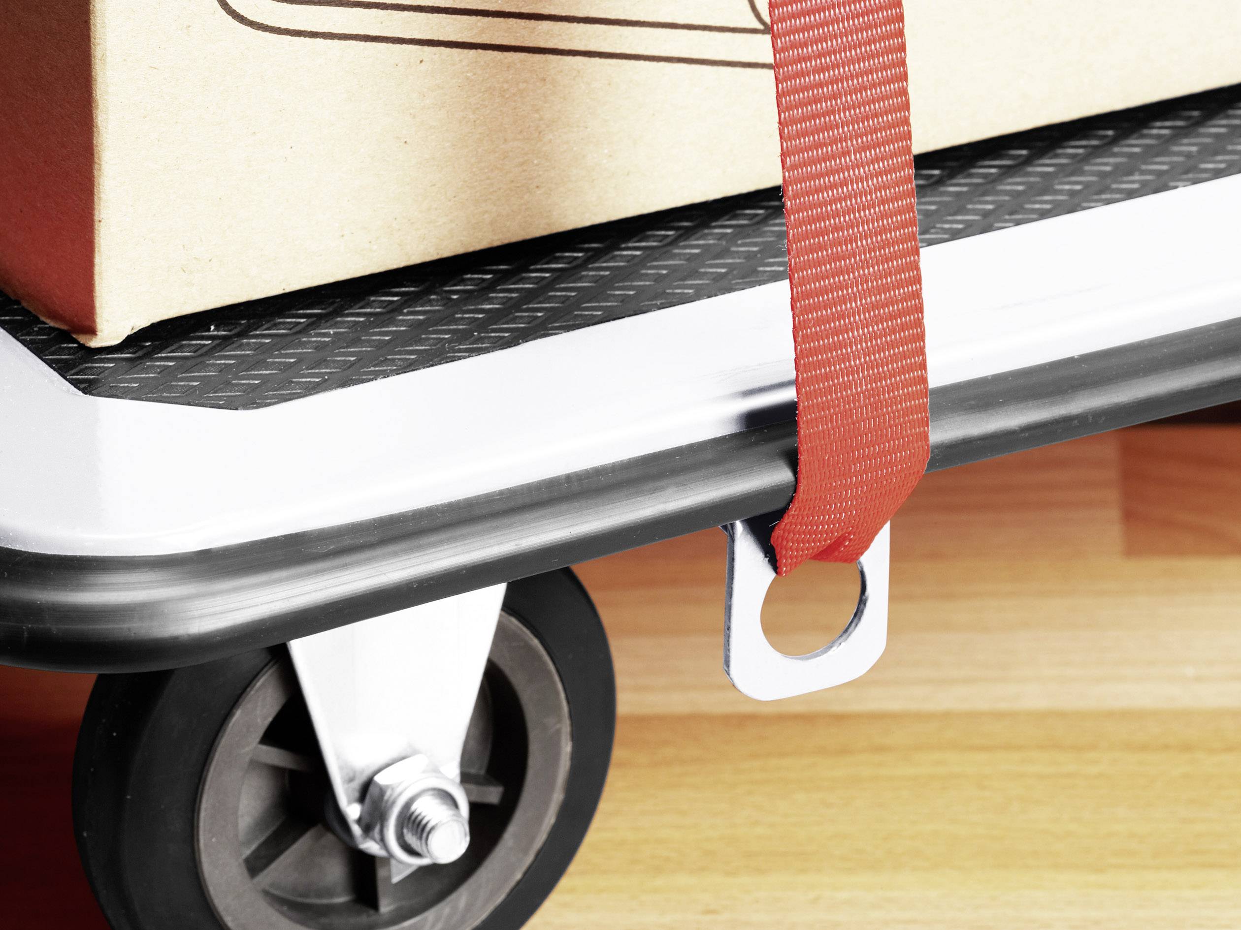 Nahaufnahme eines Rollwagens mit einer Kiste darauf, gesichert durch ein rotes Band.