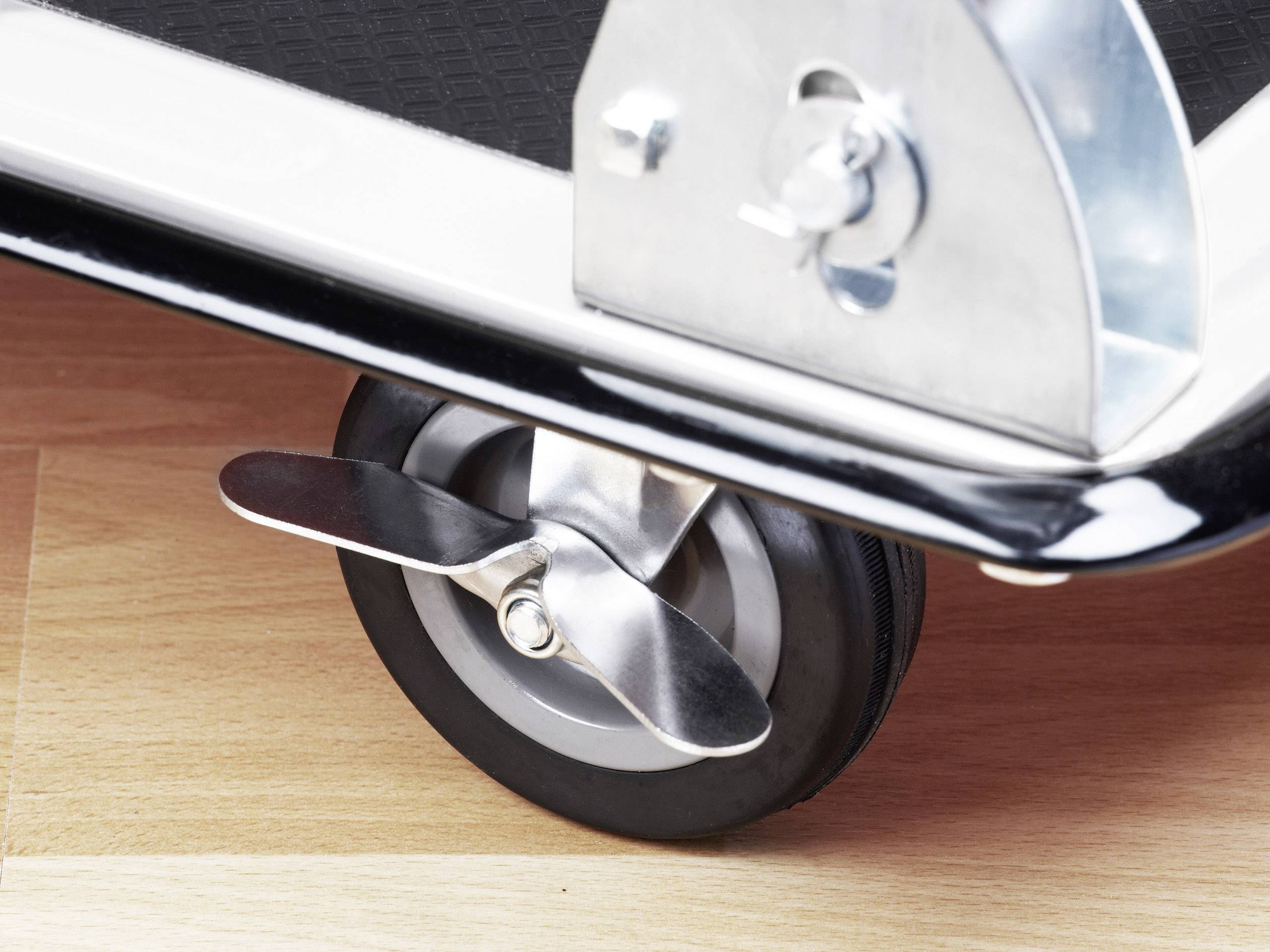 Nahaufnahme eines Metallrads mit Bremse auf Holzfußboden. Das Rad ist Teil eines Transportwagens.