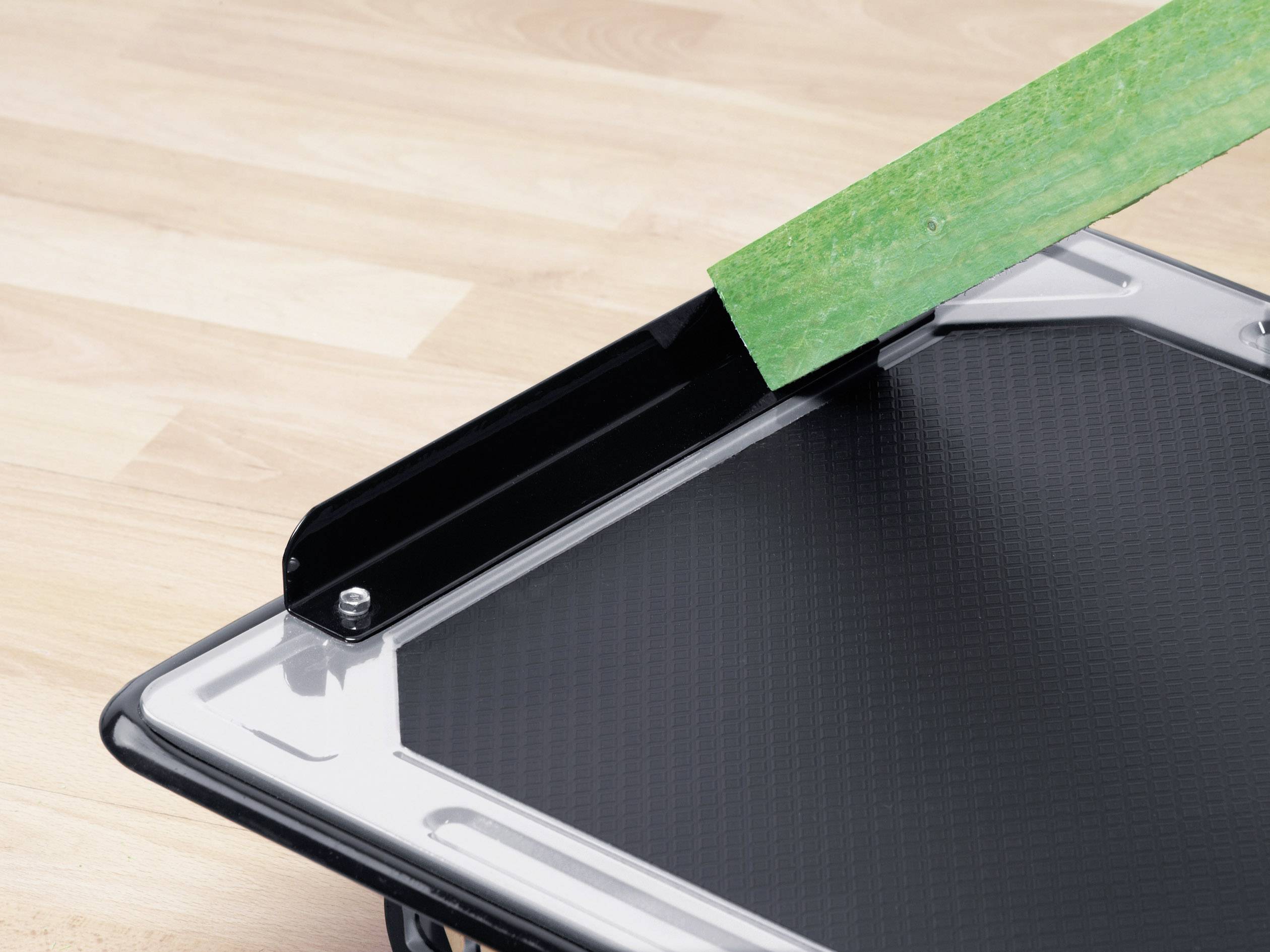 Ein schwarzes Schneidebrett mit einer Klinge, die ein grünes Material schneidet, auf einem Holztisch.