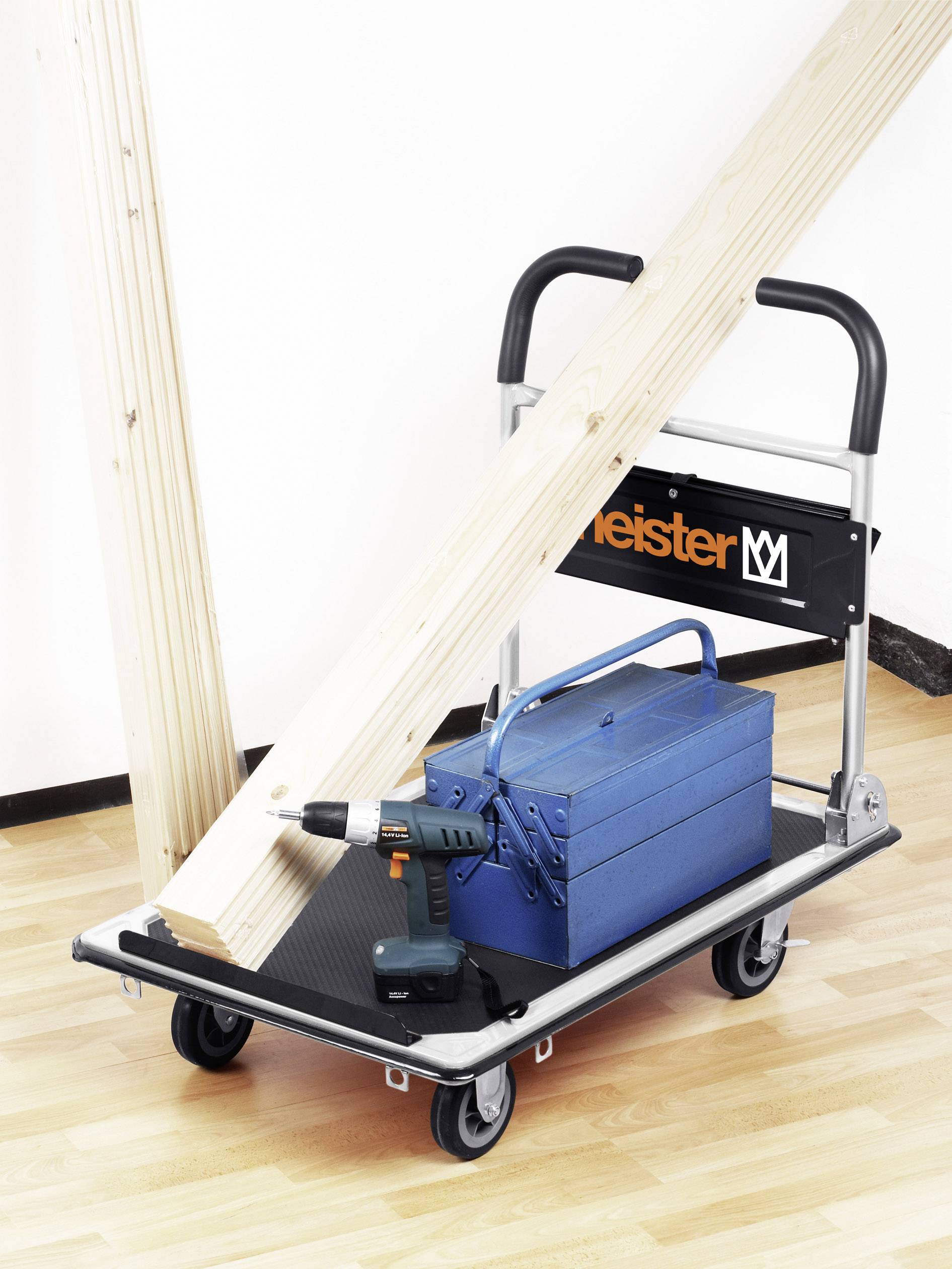 Transportwagen mit Holzbalken, blauem Werkzeugkasten und Akkubohrer auf Parkettboden.
