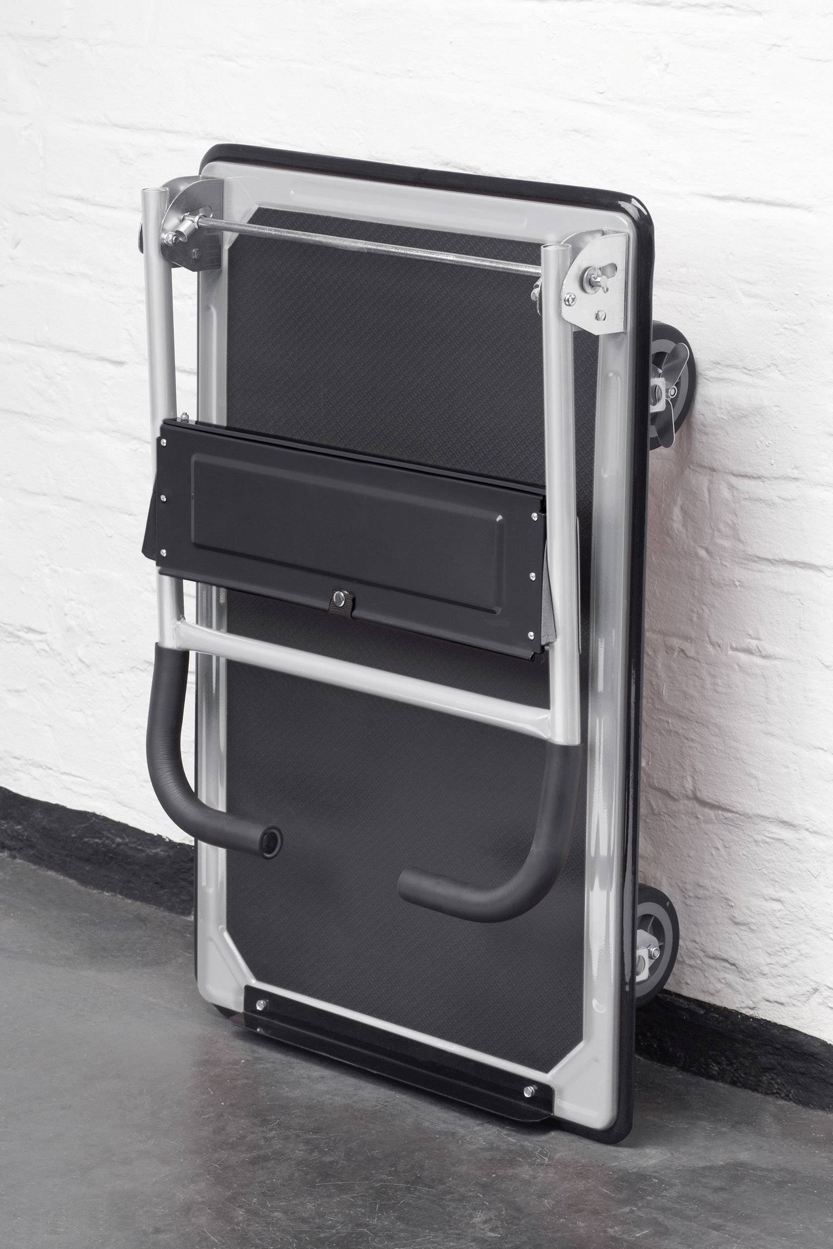 Zusammengeklappter Tisch mit Rollen lehnt an einer weißen Ziegelwand, bereit zur Lagerung oder zum Transport.