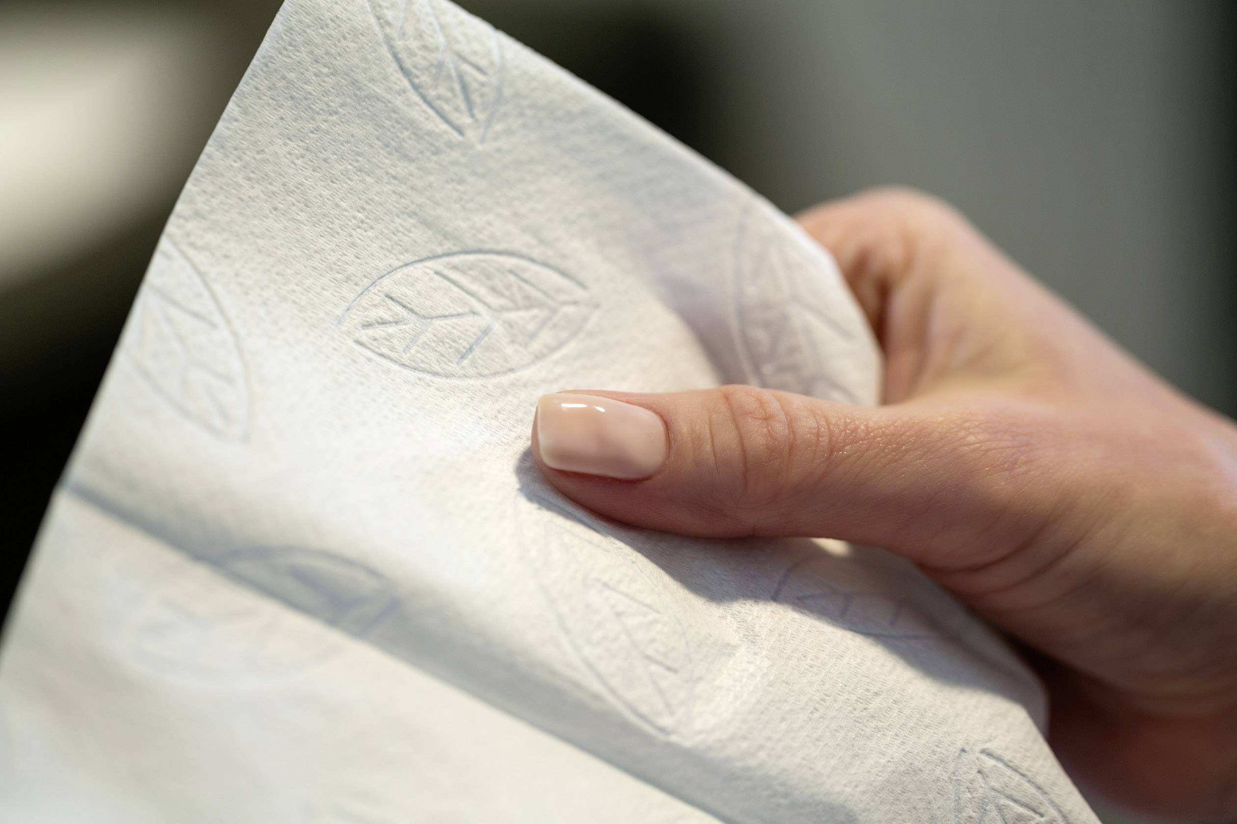 Eine Hand hält eine weiße Serviette mit Blattmustern.