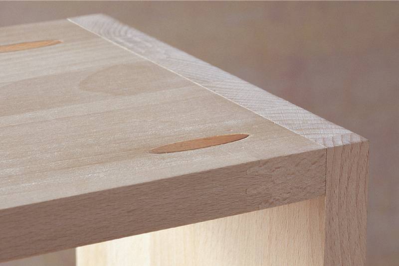 Ecke eines Holztisches mit sichtbaren Dübelverbindungen.