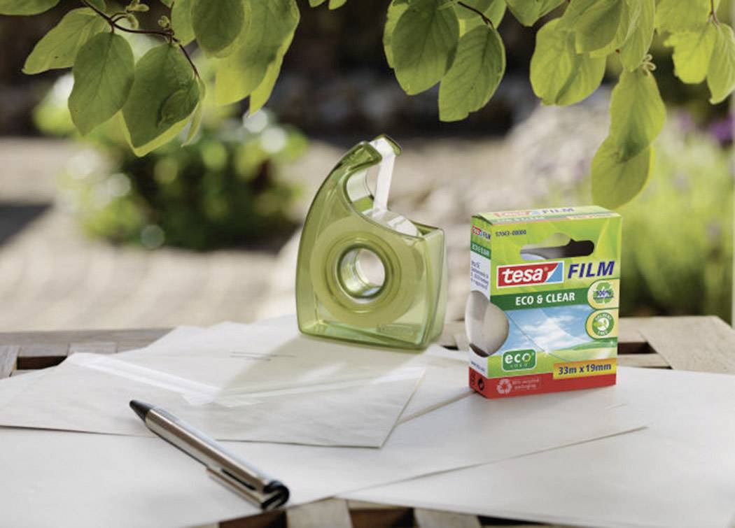 Ein Klebeband-Abroller und eine Packung 'tesa Film Eco & Clear' stehen auf einem Tisch im Freien, umgeben von Blättern und Papier.
