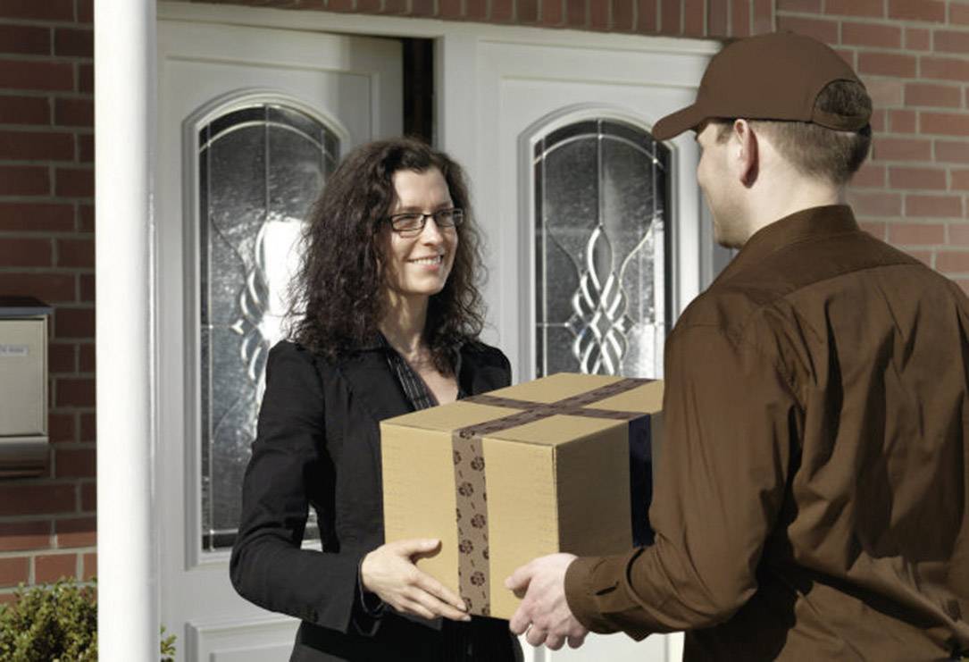 Eine Frau nimmt an der Haustür ein Paket von einem Lieferboten entgegen. Beide lächeln.