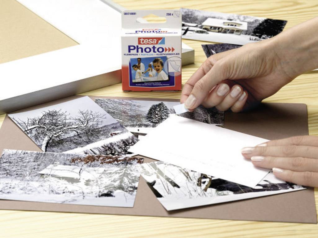 Person klebt Schwarz-Weiß-Fotos mit Tesa Photo Klebestreifen auf. Packung Tesa Photo sichtbar im Hintergrund.