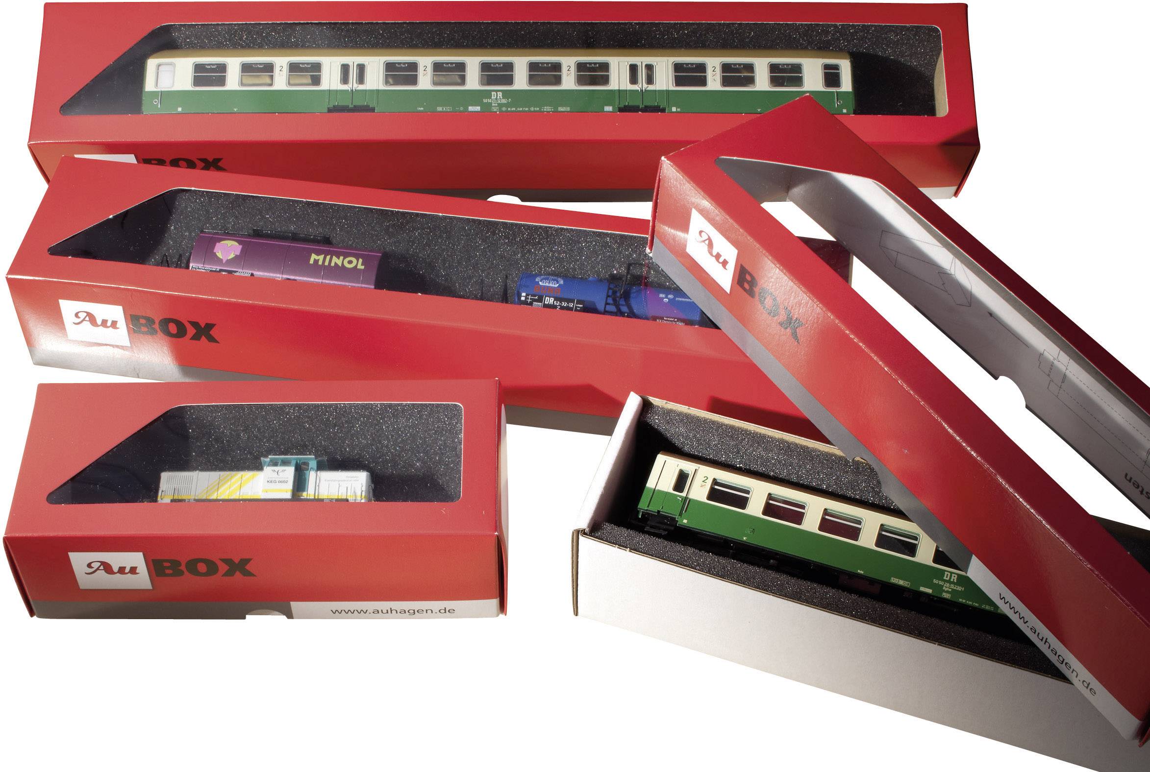 Spielzeugzugmodelle in roten Verpackungen. Verschiedene Waggons sind zu sehen, darunter ein grüner Personenwagen und ein Minol-Tankwagen.
