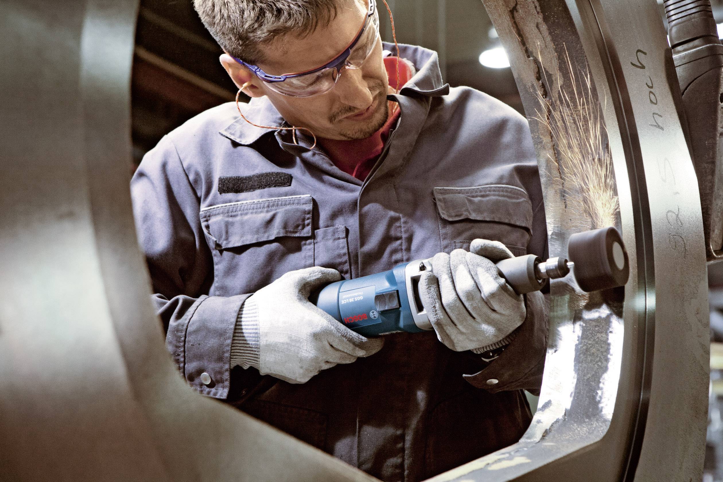 Ein Arbeiter in Schutzkleidung schleift mit einem Elektrowerkzeug die Innenseite eines großen Metallteils in einer Werkstatt.