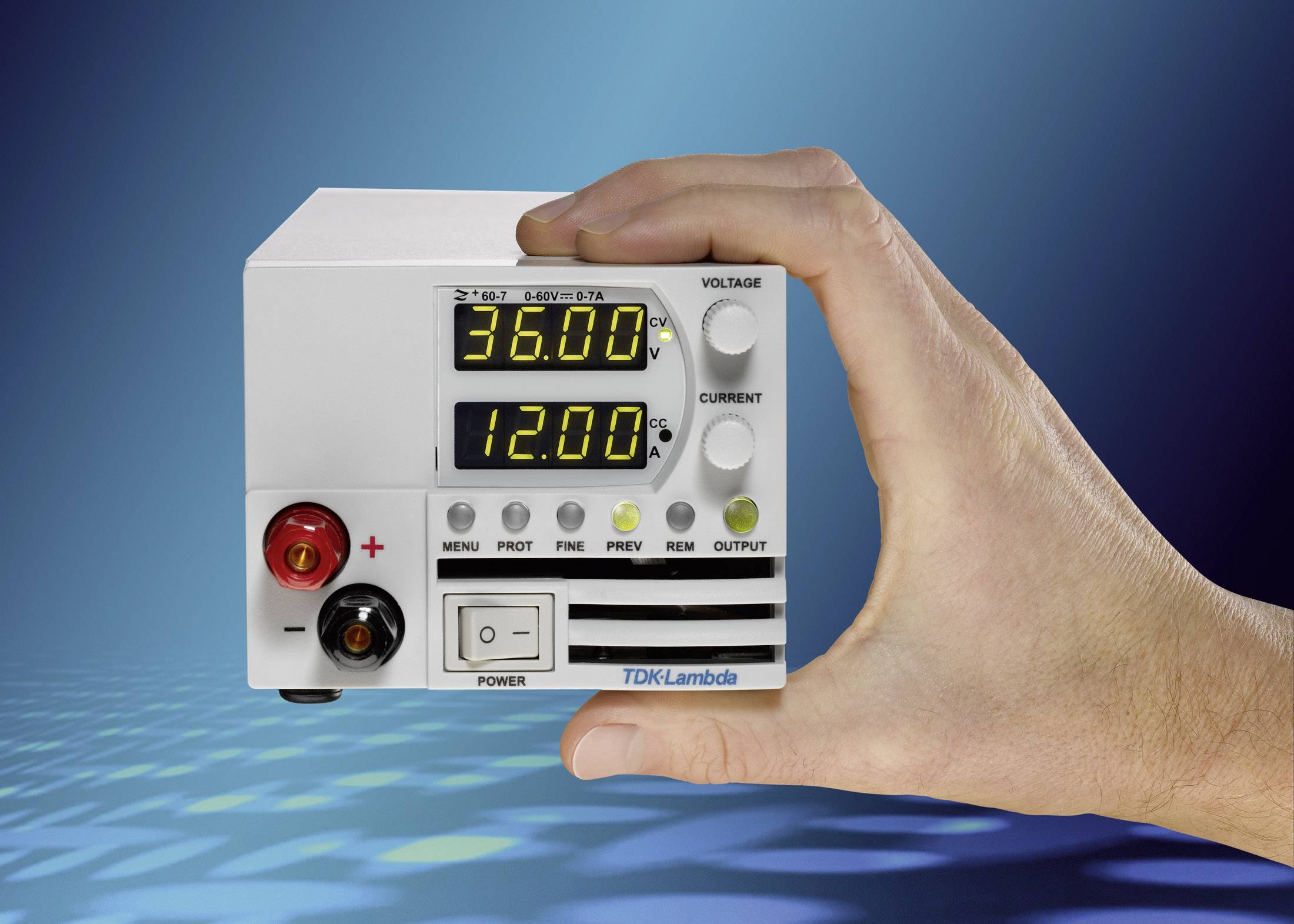 Eine Hand hält ein kleines Netzteil mit digitaler Anzeige. Die Anzeige zeigt '36,00' Volt und '12,00' Ampere.