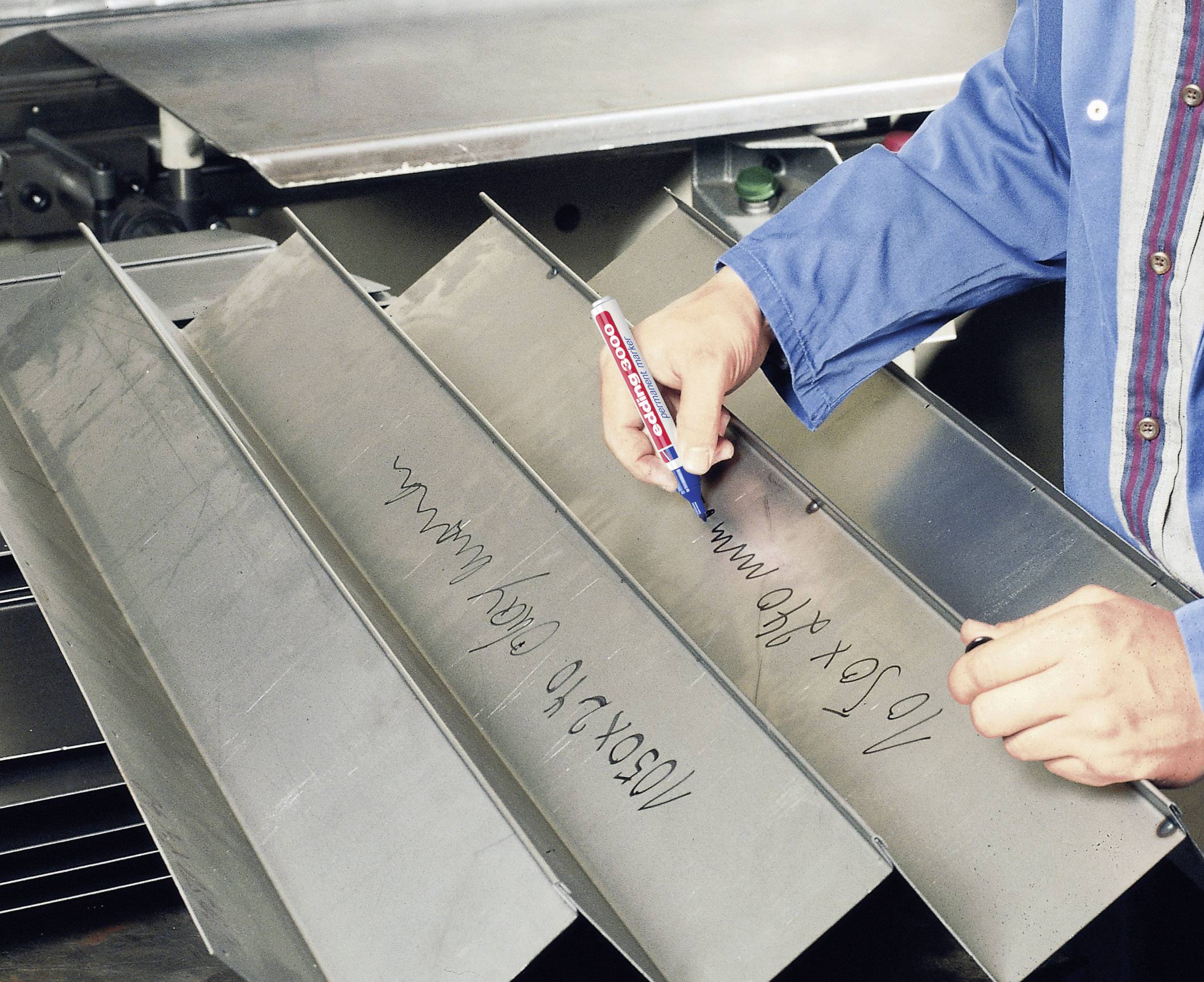 Eine Person in blauer Arbeitsjacke schreibt mit einem roten Stift mathematische Formeln auf metallische Platten.
