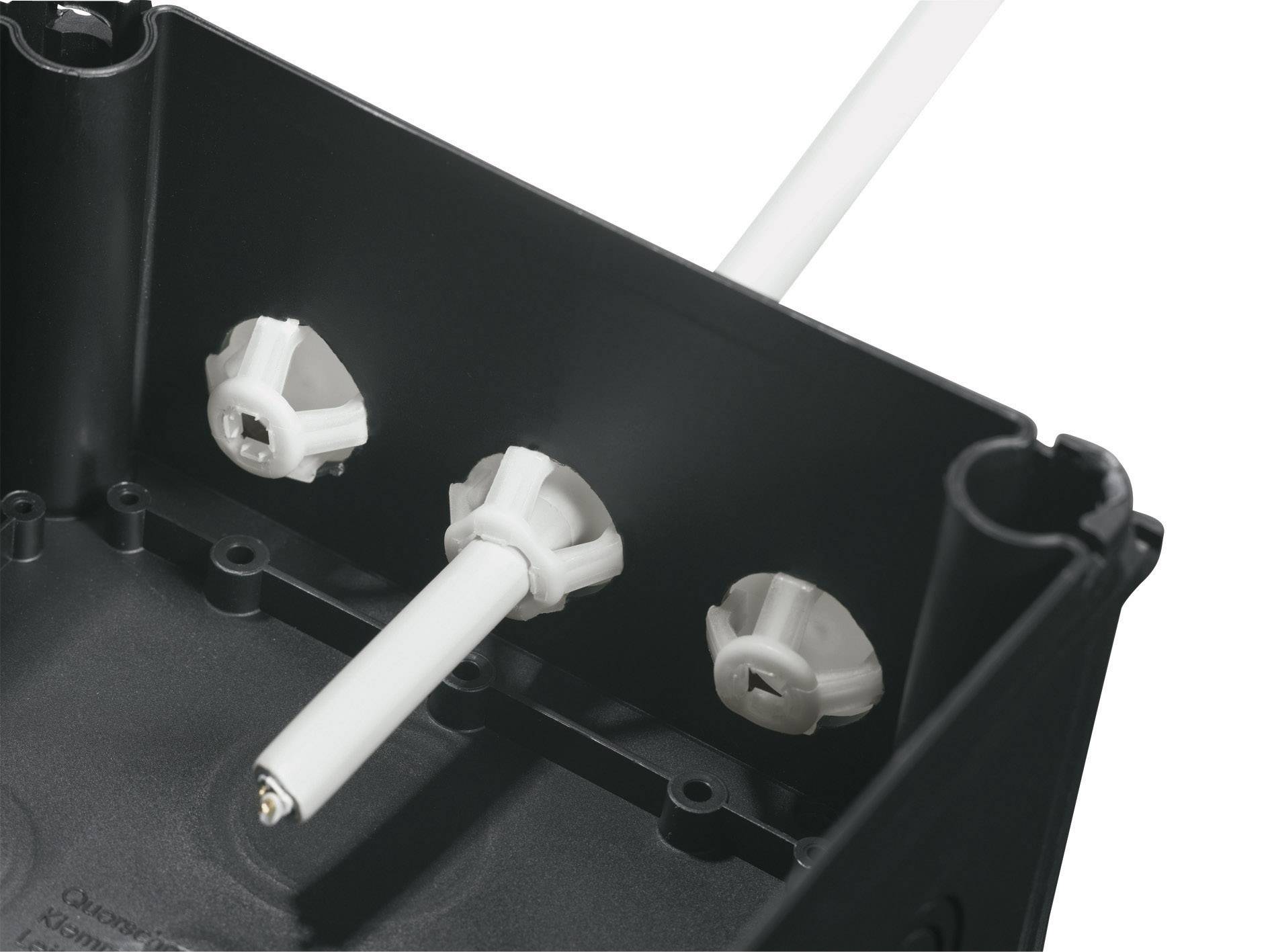 Nahaufnahme eines schwarzen Gehäuses mit drei weißen Plastikbefestigungen und einem Kabel, das aus einer Halterung herausragt.