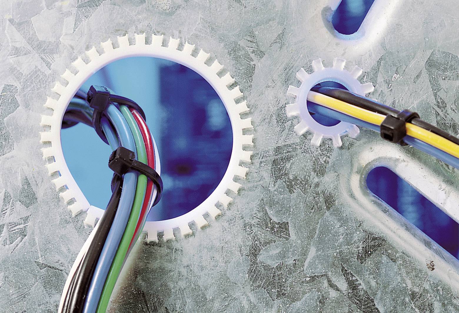 Kabelbündel führen durch Metallscheiben in einer blauen Oberfläche. Verschiedene Kabelbinder sichern die Kabel.