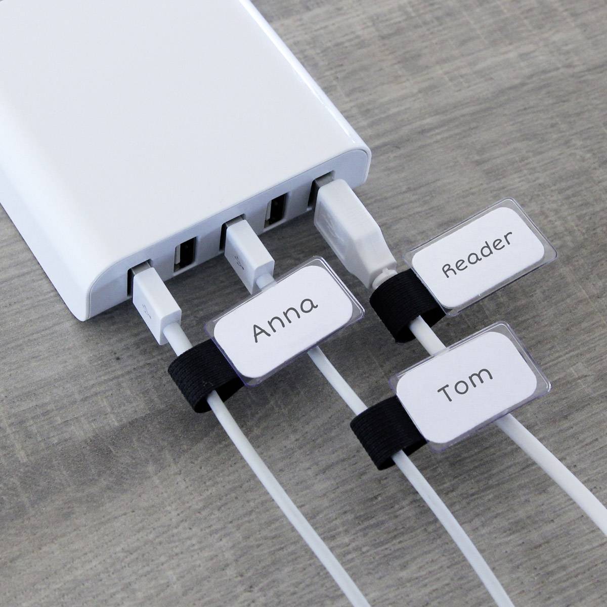 Ein Ladegerät mit vier USB-Anschlüssen lädt drei Geräte. Die Kabel sind beschriftet mit 'Anna', 'Reader' und 'Tom'.