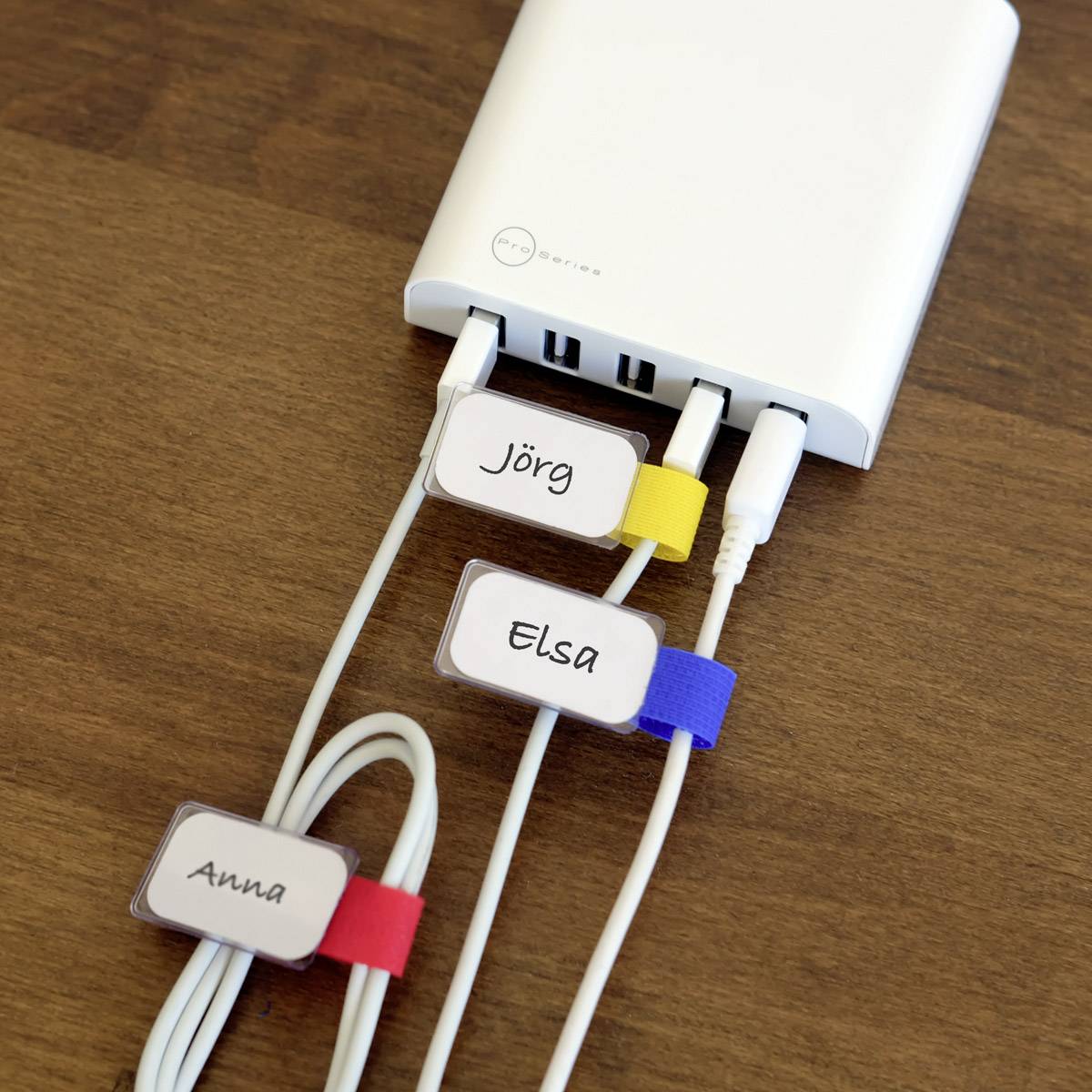 Drei Kabel sind an ein Ladegerät angeschlossen. Jedes Kabel ist mit einem farbigen Etikett beschriftet: 'Jörg', 'Elsa', 'Anna'.