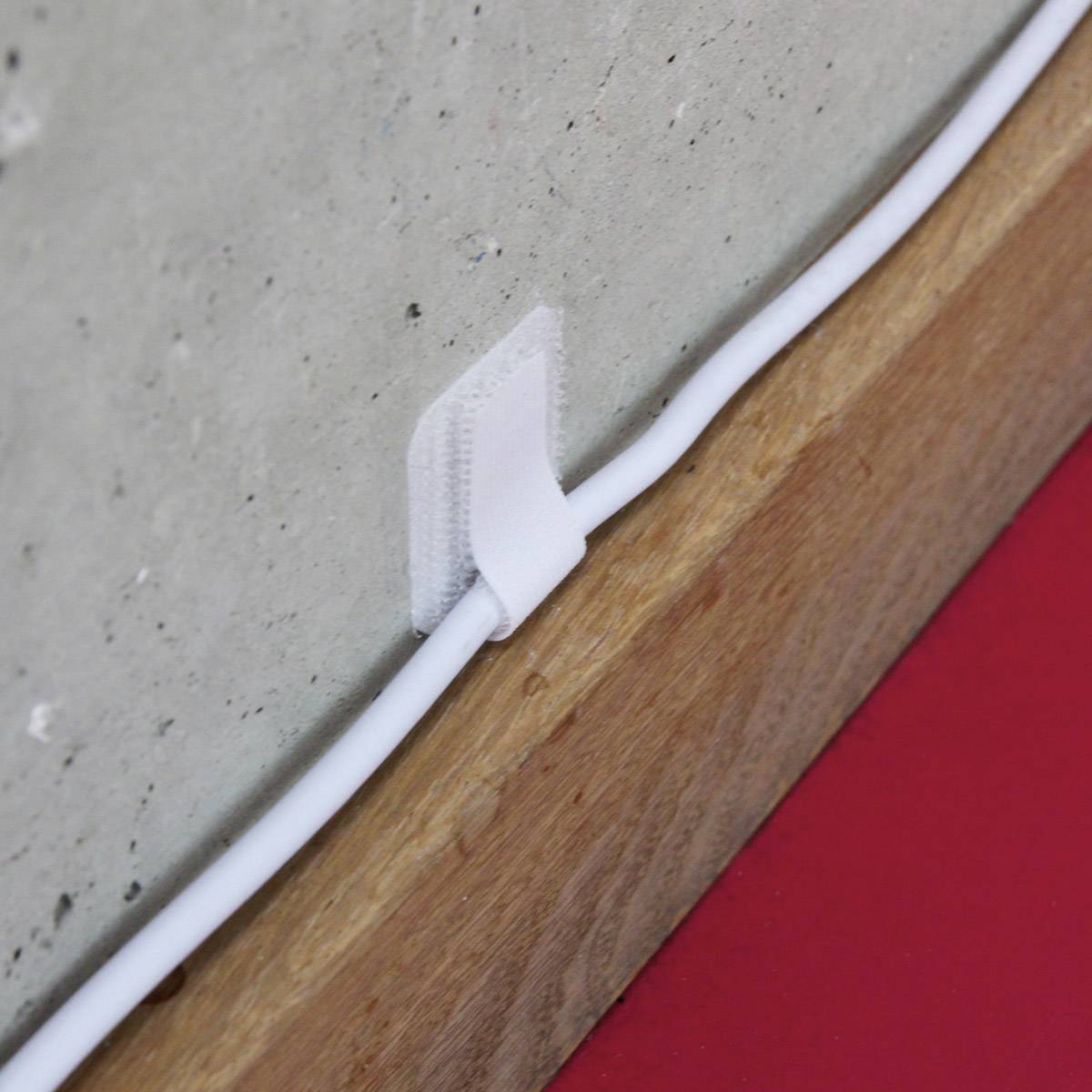 Ein Kabel wird mit einem weißen Klettband an einer Wand entlanggeführt.