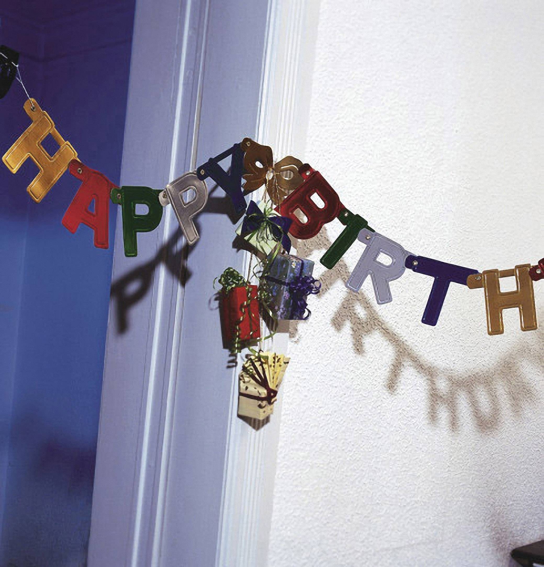 Banner mit bunten Buchstaben, die 'HAPPY BIRTHDAY' buchstabieren, hängt diagonal an der Wand. Im Hintergrund sind Schatten sichtbar.