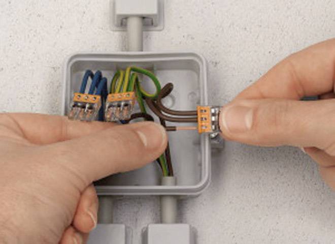 Eine Person verbindet Kabel in einer grauen Anschlusdose. Mehrfarbige Kabel sind mit Steckverbindern verbunden.