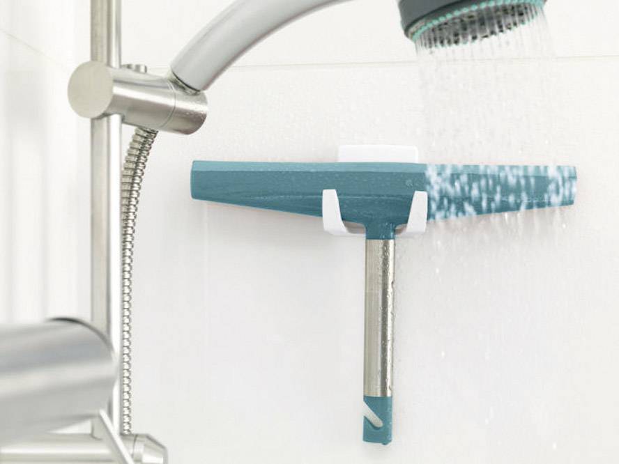 Ein Duschabzieher hängt an einer Duschwand, während Wasser darauf sprüht. Er hat einen blauen Griff und ist in einer Halterung befestigt.