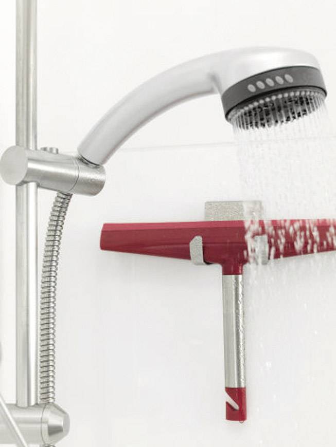 Eine Handbrause mit Wasserstrahl trifft auf einen Scheibenabzieher, der an einer Halterung in einem Duschraum befestigt ist.