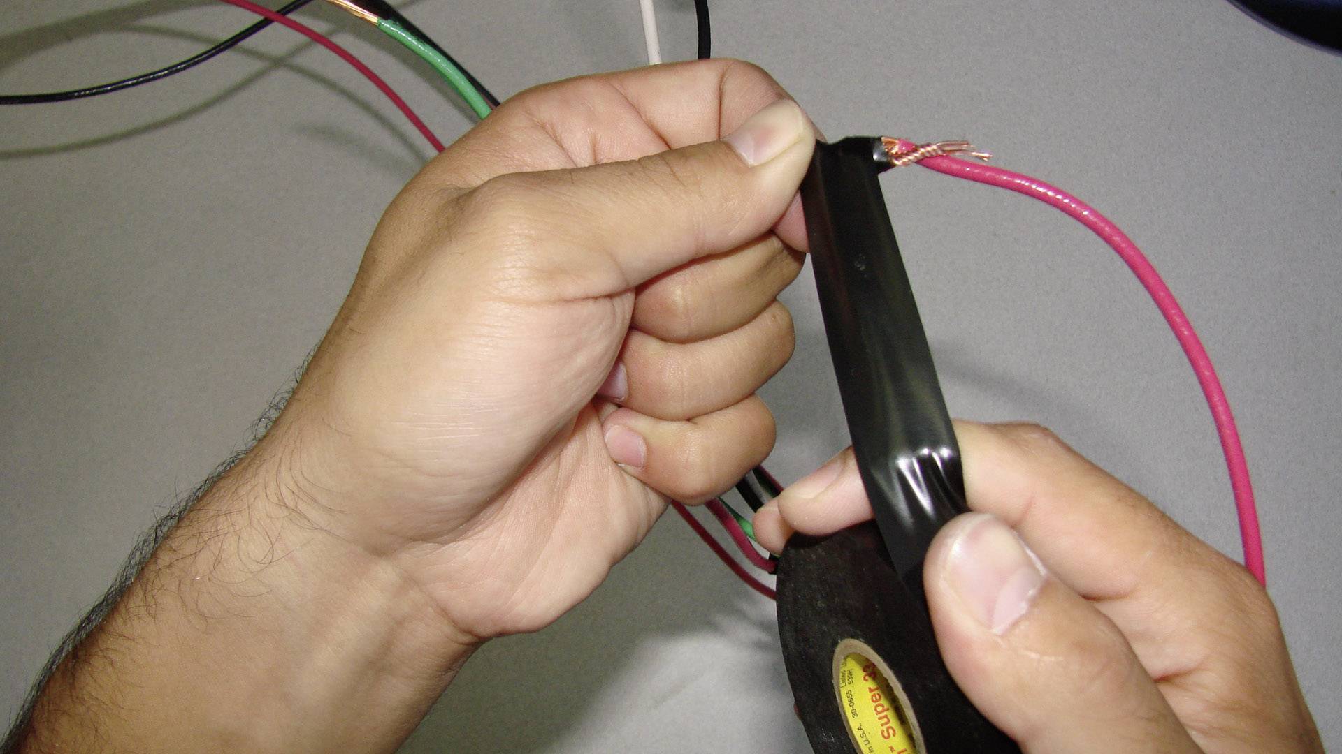 Hände wickeln schwarzes Isolierband um ein freiliegendes Kabel, um es zu reparieren oder zu isolieren.