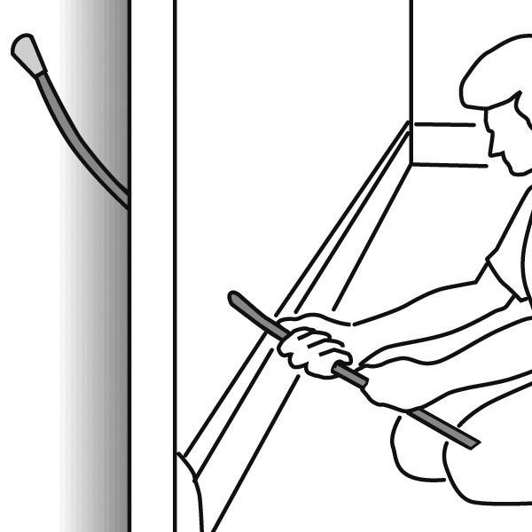 Eine Person kniet am Boden und benutzt ein Werkzeug, um Kabel in einen Kabelkanal an der Wand einzuführen.